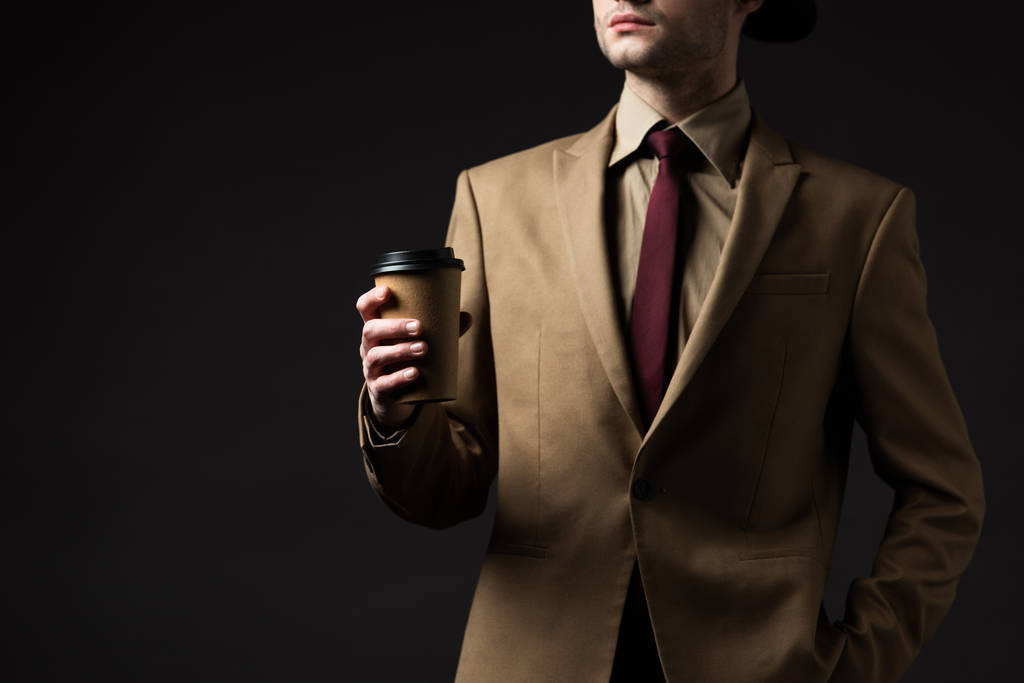 περικοπή άποψη του κομψού άνδρα σε μπεζ κοστούμι κρατώντας κύπελλο χαρτί απομονώνονται σε μαύρο - Φωτογραφία, εικόνα