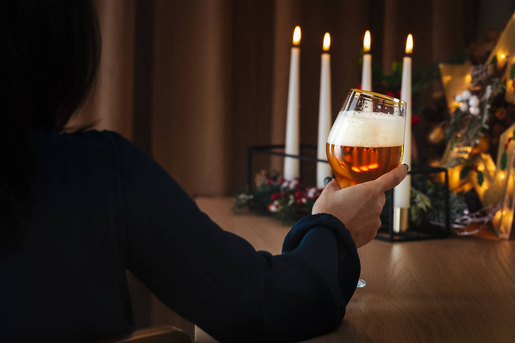 Jovem fêmea segurando copo de cerveja em atmosfera romântica com luz de vela
. - Foto, Imagem
