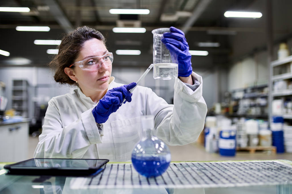 Jonge laboratoriumassistent met fles en tablet in handen - Foto, afbeelding