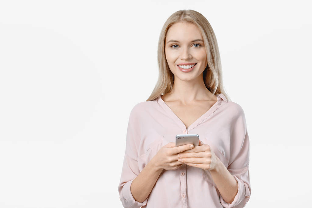 Porträt einer lächelnden Frau, die lässig ihr Smartphone vor weißem Hintergrund benutzt - Foto, Bild