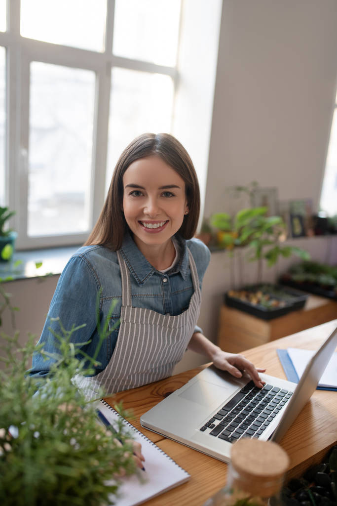 Glimlachende vrouw werkt met een computer in een plantenwinkel - Foto, afbeelding
