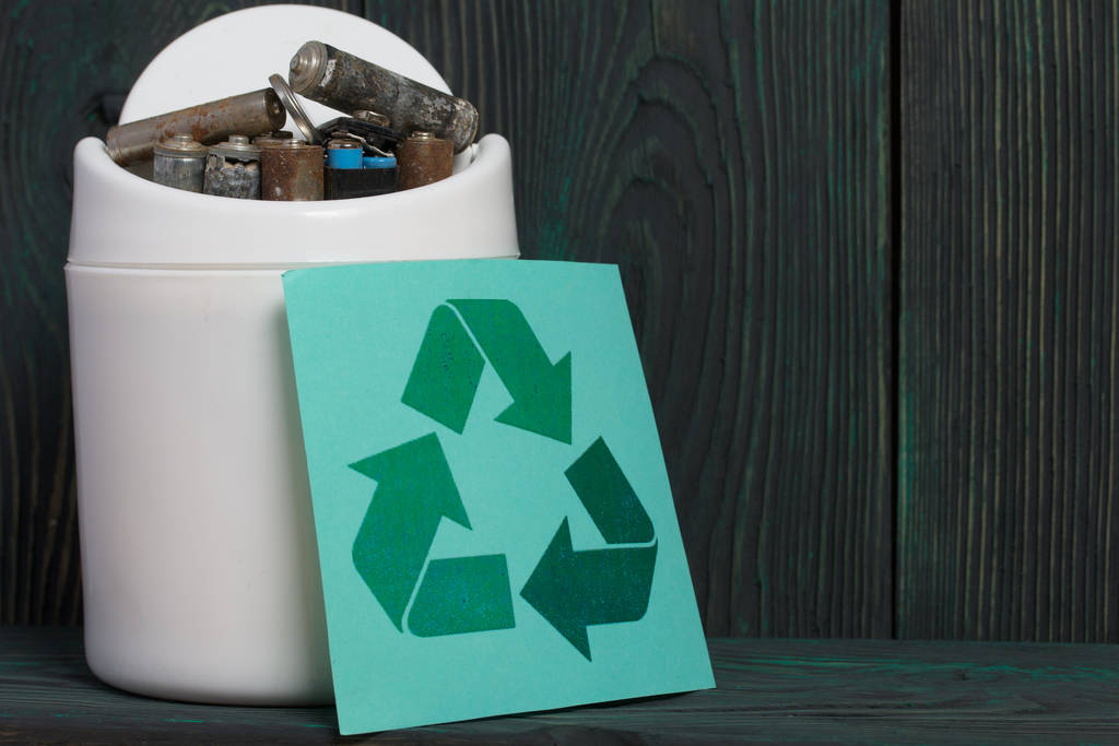 ゴミ箱だ腐食でコーティングされた指型電池が含まれています。近くには廃棄物リサイクルの看板があります。黒と緑に塗られた松の板の上に横たわる。. - 写真・画像