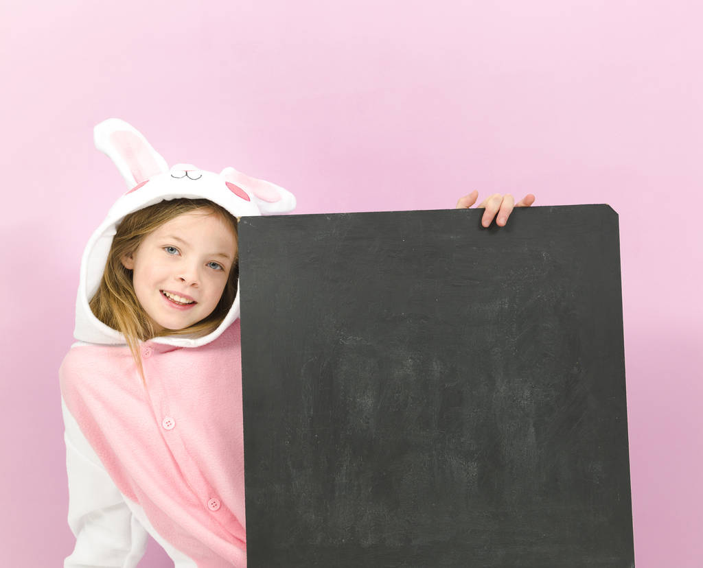 šťastný pěkný blondýny dívka v útulný králík kostým s prázdnou tabulí pózování ve studiu  - Fotografie, Obrázek