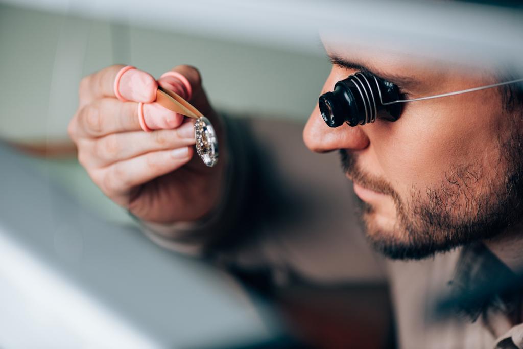 Vista lateral del guapo relojero en lupa de anteojos mirando la pieza del reloj de pulsera
  - Foto, imagen