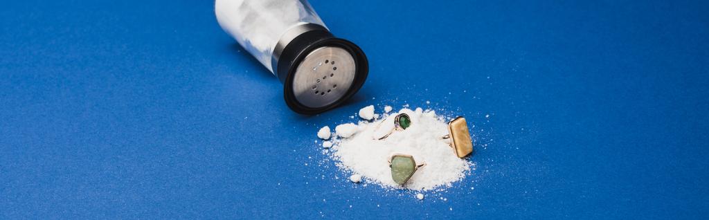 Панорамный снимок солонки с помощью ювелирных колец на куче соли на синем фоне
 - Фото, изображение