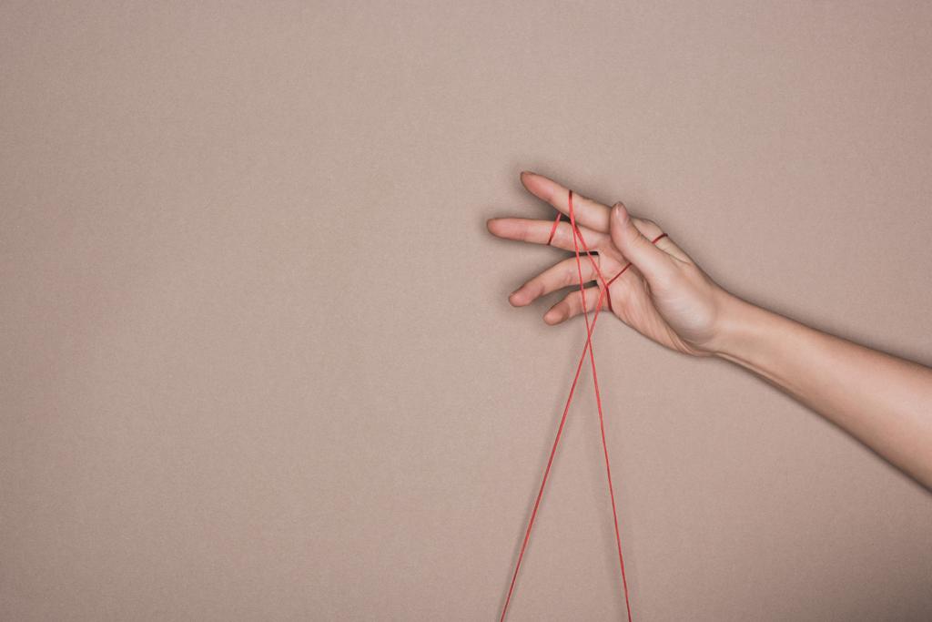 Вид сверху женской руки с красной нитью на бежевом фоне
 - Фото, изображение
