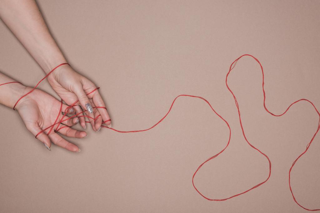 Top nézet a női kéz csomagolva piros húr bézs háttér - Fotó, kép