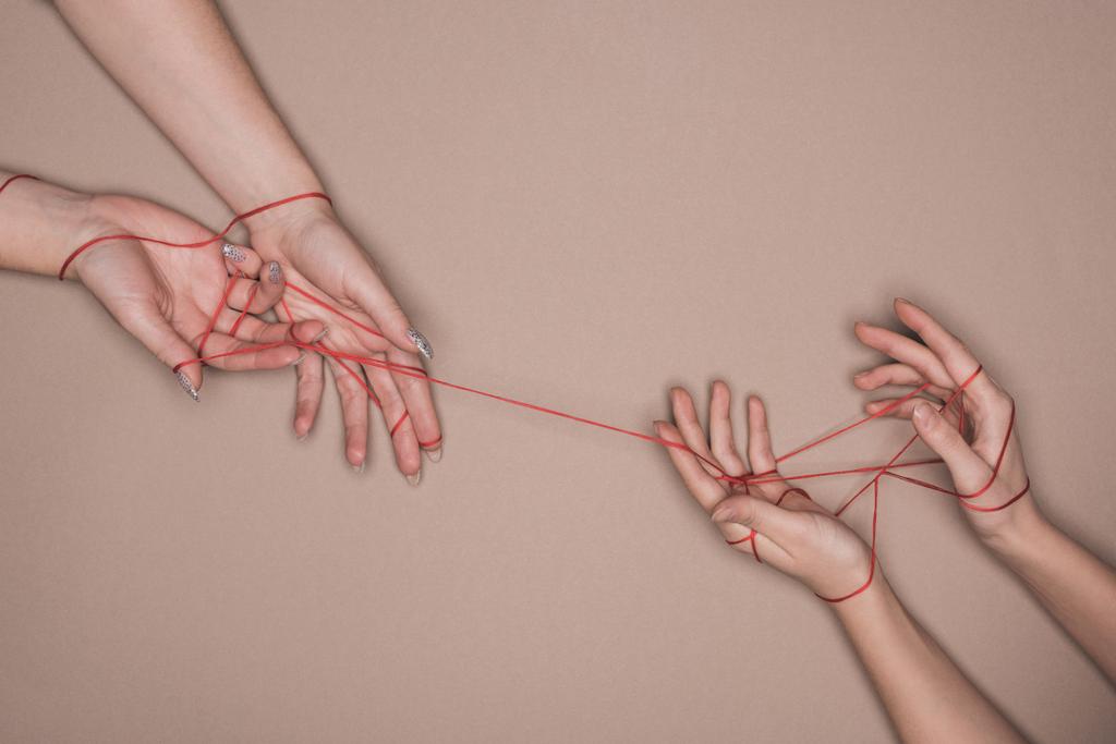 Vue du dessus des mains des femmes enveloppées de fil rouge sur fond beige
 - Photo, image