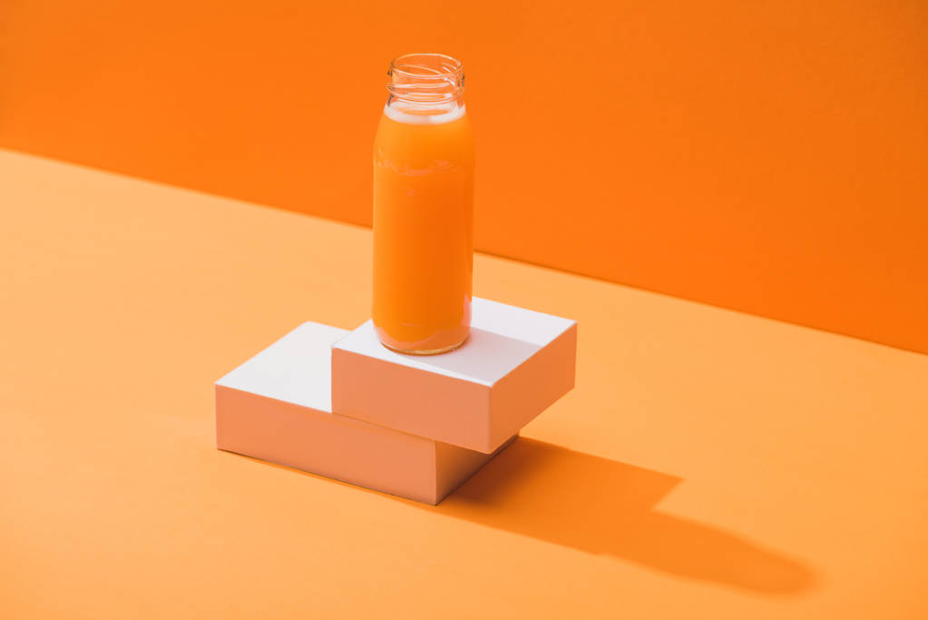 Cam şişede taze havuç suyu turuncu arka planda küp şeklinde. - Fotoğraf, Görsel