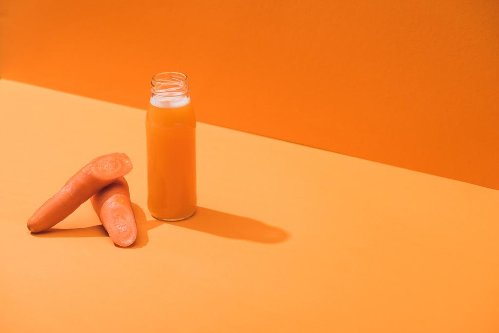 fresh juice in glass bottle near ripe carrots on orange background - Photo, Image
