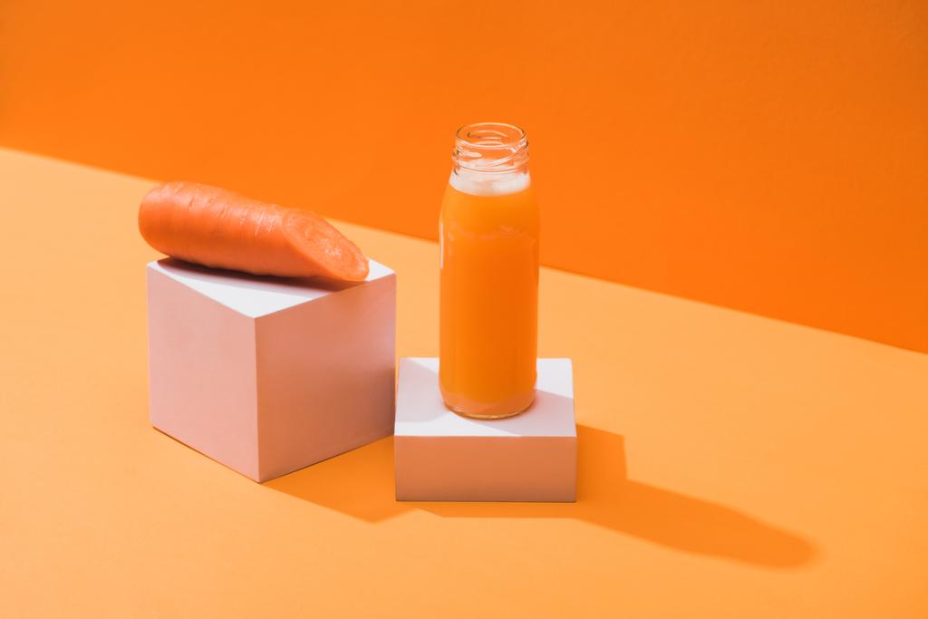 zumo fresco en botella de vidrio cerca de zanahoria madura en cubos sobre fondo naranja
 - Foto, imagen