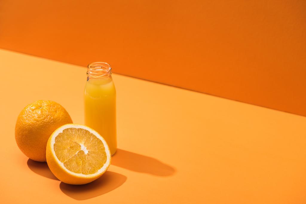 zumo fresco en botella de vidrio cerca de naranjas sobre fondo naranja
 - Foto, Imagen