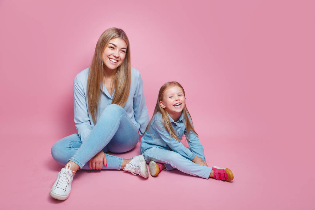 Moeder en weinig dragen blauwe shirts zittend op fel roze achtergrond - Foto, afbeelding
