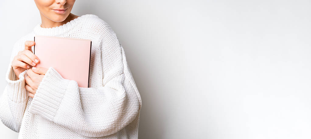 Close view van vrouw in witte wollen trui met een boek met lege roze omslag in handen. Vrije ruimte voor uw maquette van het leesboek concept achtergrond. - Foto, afbeelding