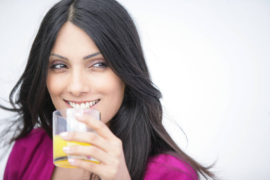 Portret van een lachende vrouw met een glas sinaasappelsap in de hand - Foto, afbeelding