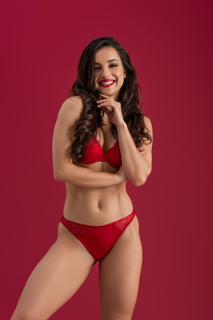seductive girl in lingerie smiling at camera while standing isolated on red - Photo, Image