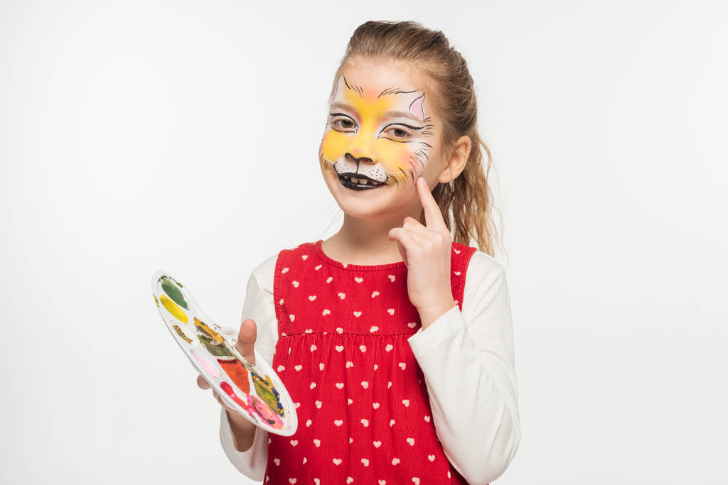 lachend kind met tijgermuilkorf op het gezichtspalet en wijzend met de vinger naar gezicht geïsoleerd op wit - Foto, afbeelding