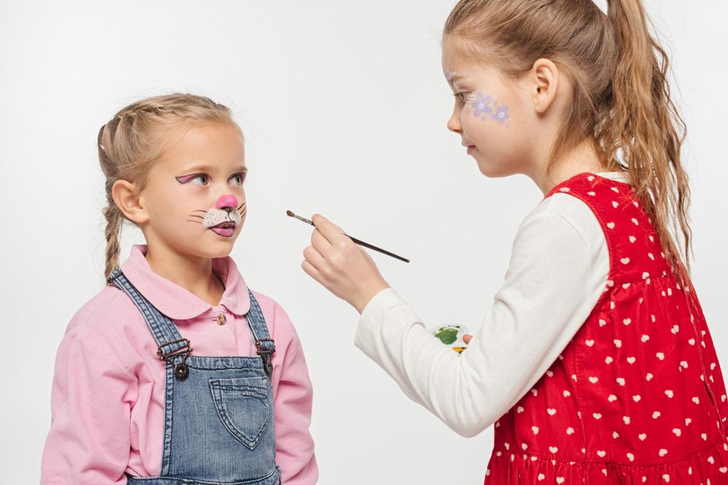 cute child with floral pattern on face holding paintbrush near friend with painted cat muzzle isolated on white - Photo, Image
