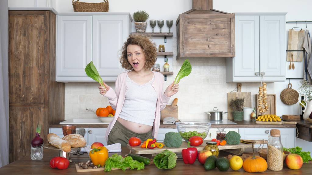 Onnellinen raskaus nainen tanssia vihreää salaattia keittiössä
 - Valokuva, kuva
