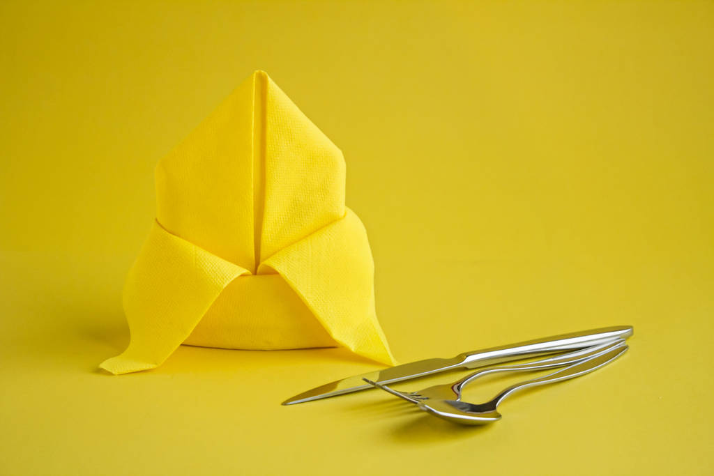 Nahaufnahme einer gefalteten gelben Serviette für schöne Tischdekoration und Utensilien auf gelb - Foto, Bild