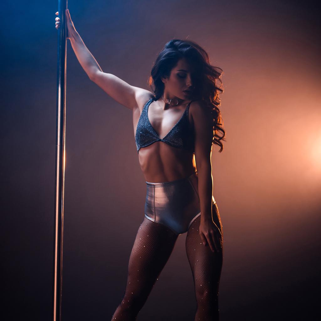 sexy stripper en undrewear de pie cerca de pilón mientras baila striptease en negro y naranja
  - Foto, Imagen