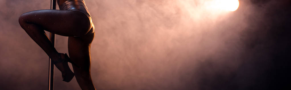 Balıkçı taytlı striptizcinin panoramik çekimi. Siyah direğin yanında dumanla striptiz yapıyor.  - Fotoğraf, Görsel