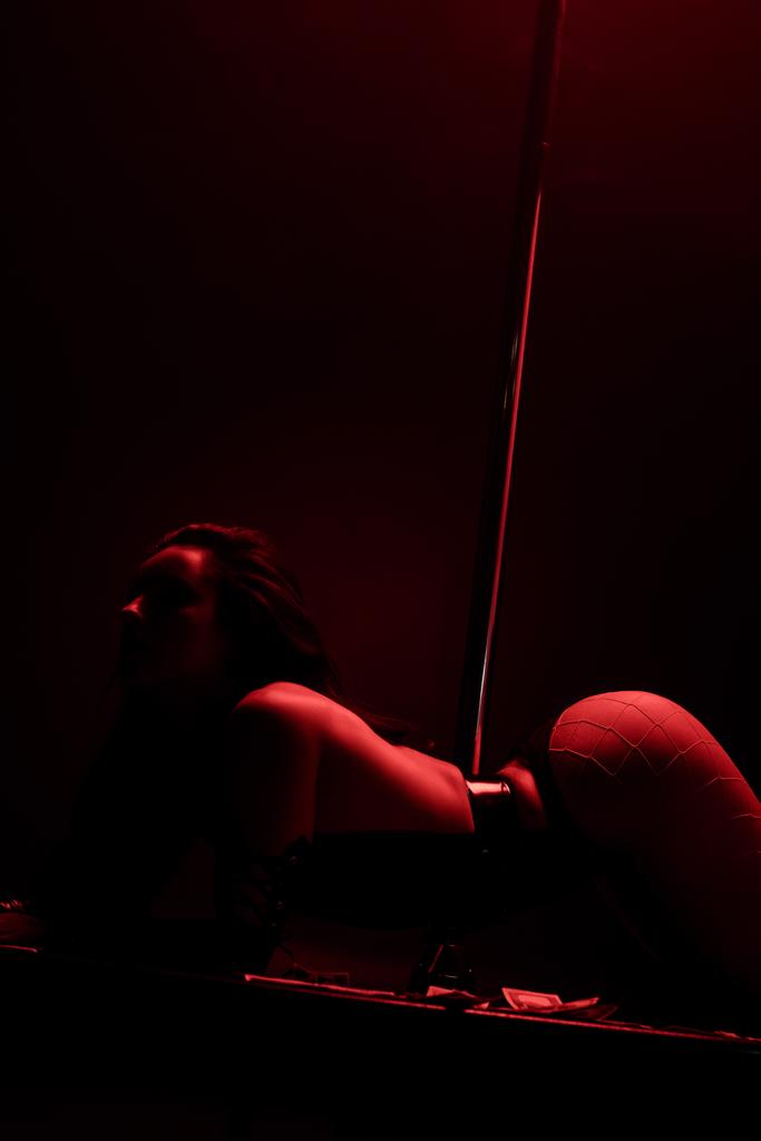 Leidenschaftliche Frau tanzt Striptease in der Nähe von Dollarnoten auf schwarz mit roter Beleuchtung  - Foto, Bild