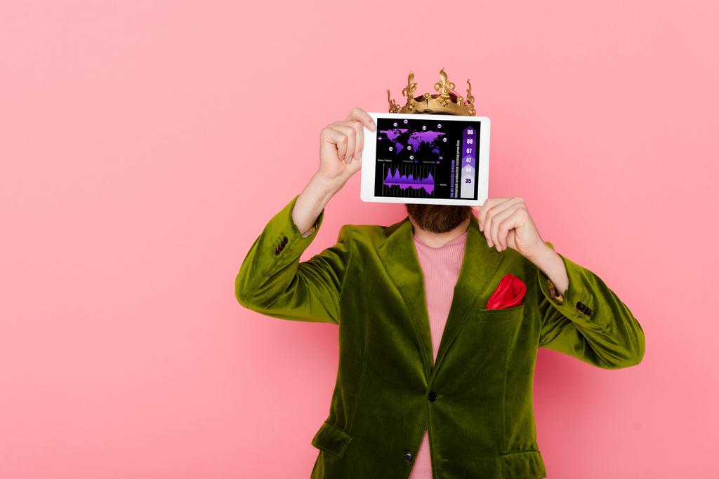 άνθρωπος με στέμμα που κατέχουν ψηφιακή ταμπλέτα με online εφαρμογή επιχειρηματικό τμήμα απομονώνονται σε ροζ - Φωτογραφία, εικόνα