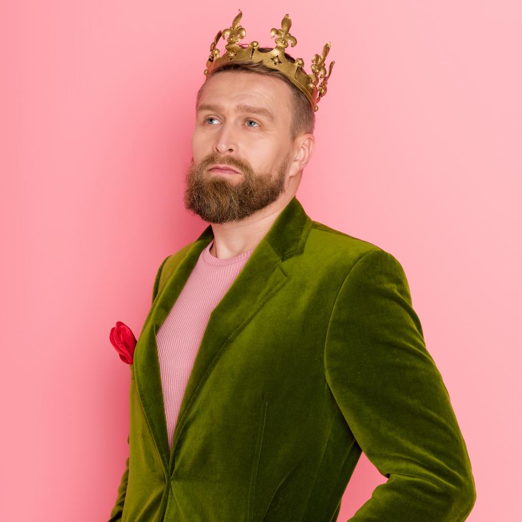 hombre guapo con corona en chaqueta de terciopelo mirando hacia otro lado sobre fondo rosa
  - Foto, imagen