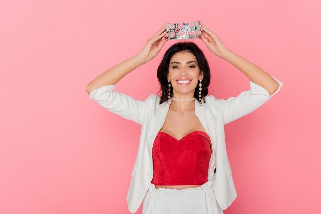 usmívající se žena drží korunu nad hlavou na růžovém pozadí  - Fotografie, Obrázek