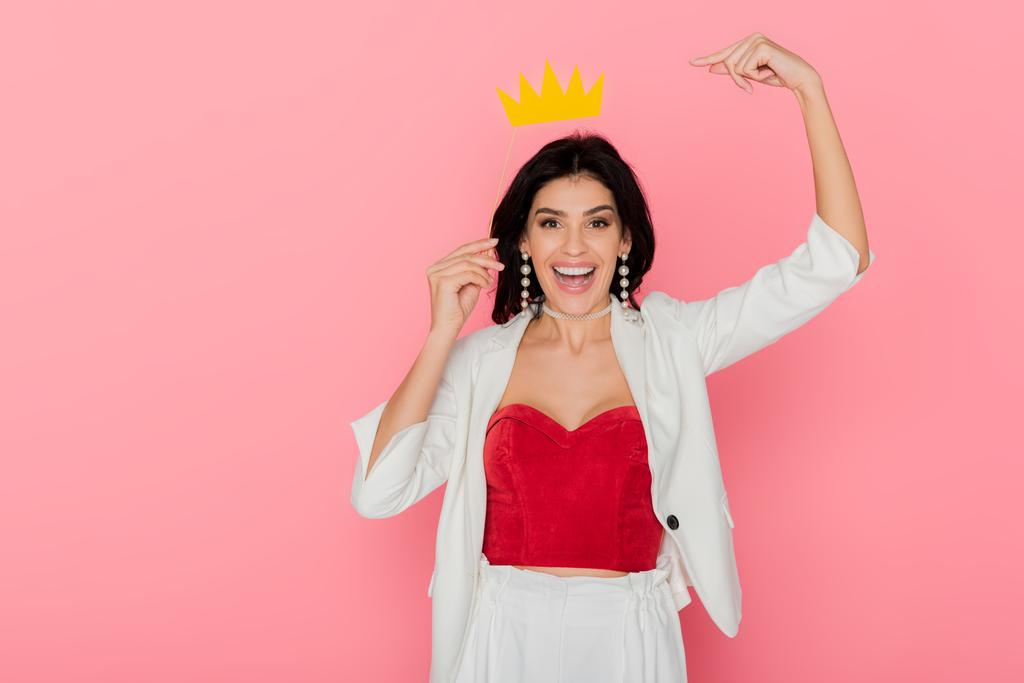 smiling woman pointing with finger at paper crown on pink background  - Photo, Image