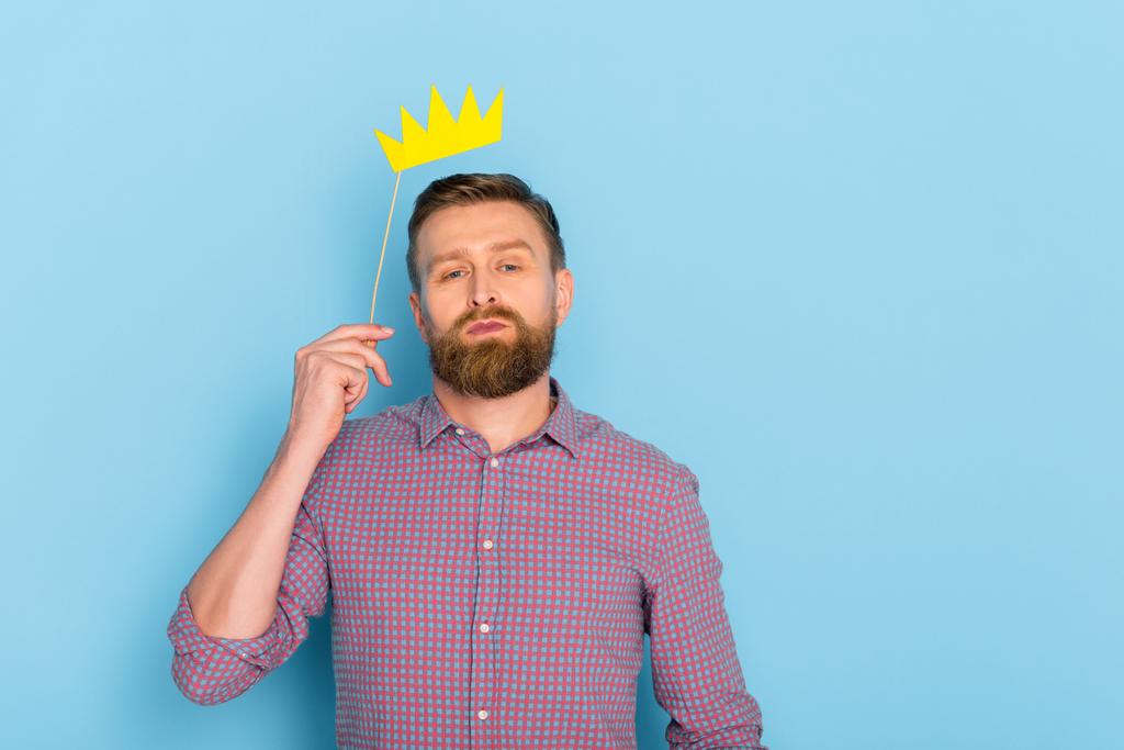 handsome man in shirt holding paper crown on blue background  - Photo, Image