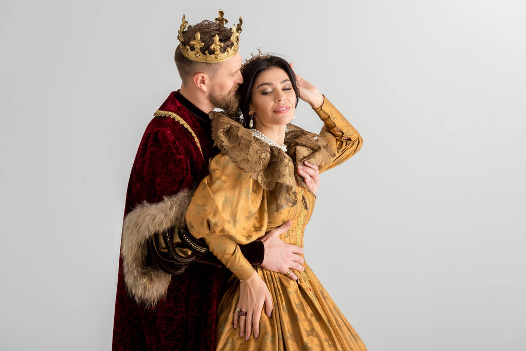 rei com a coroa beijando e abraçando a rainha sorridente isolado em cinza
 - Foto, Imagem