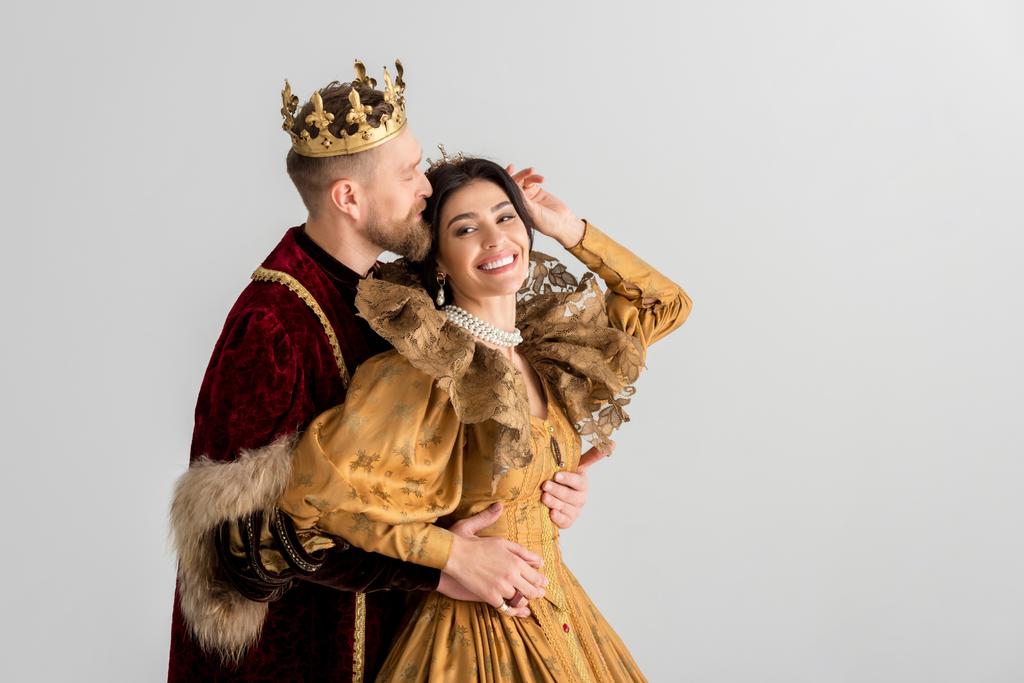 rey con corona besándose y abrazando sonriente reina aislada en gris
 - Foto, imagen