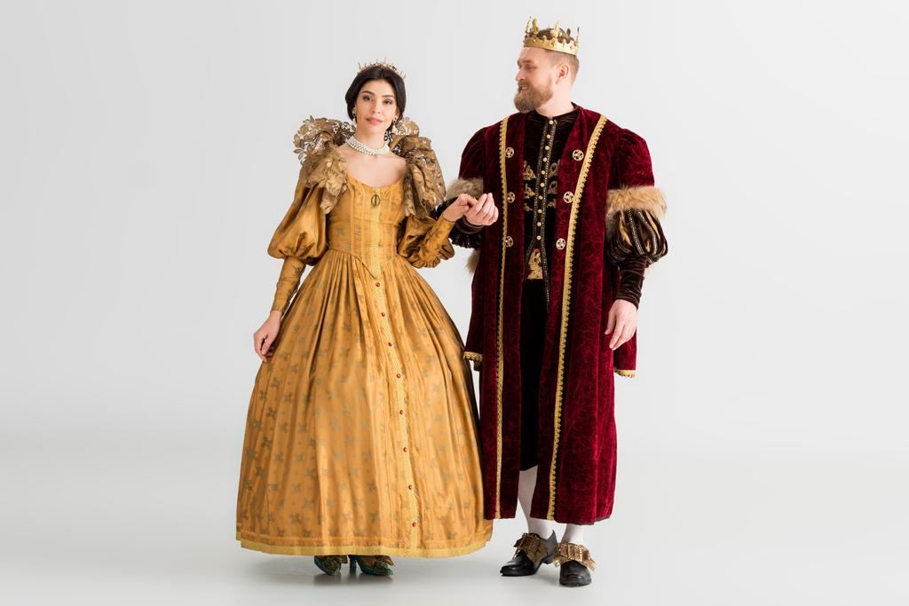 Lächelnde Königin und König mit Kronen Händchen haltend auf grauem Hintergrund  - Foto, Bild