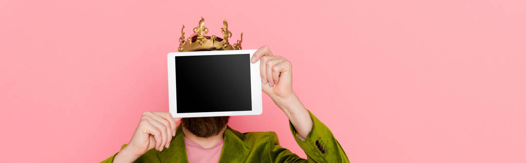 panoramic shot of man with crown holding digital tablet isolated on pink  - 写真・画像
