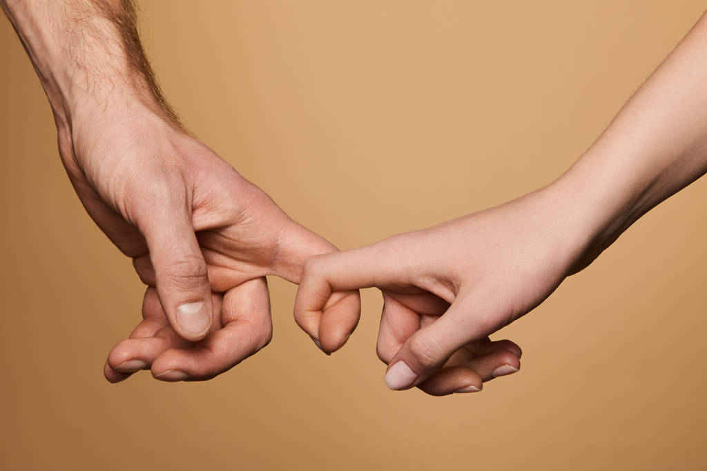 bijgesneden beeld van man en vrouw houden vingers geïsoleerd op beige - Foto, afbeelding