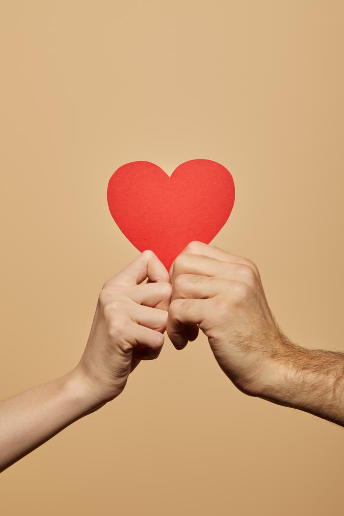 vue recadrée de l'homme et de la femme tenant le cœur rouge isolé sur beige
 - Photo, image