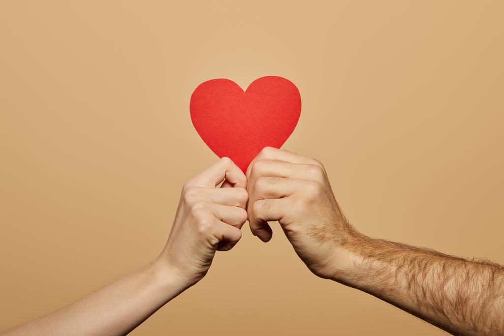 bijgesneden beeld van man en vrouw met rood hart geïsoleerd op beige - Foto, afbeelding