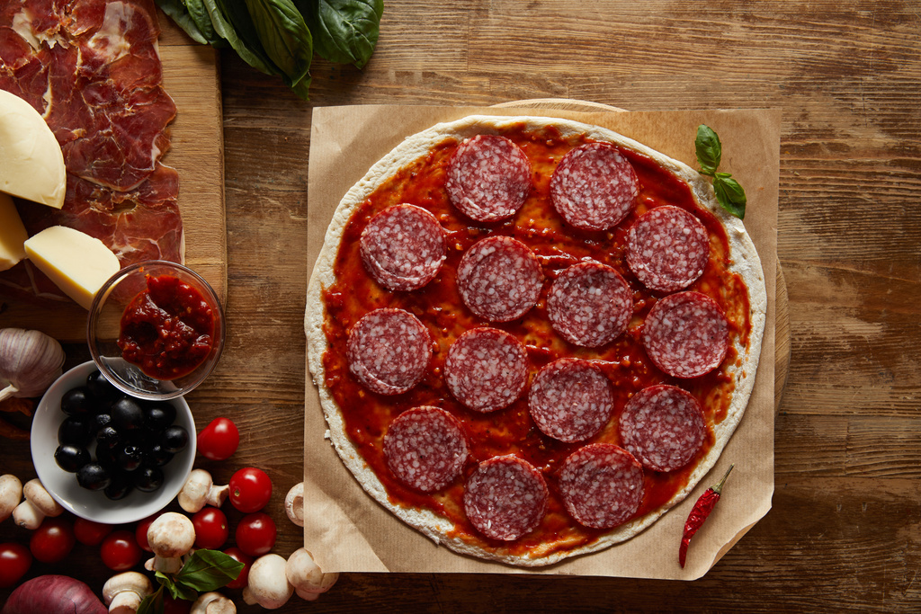Top view of pizza with salami and tomato sauce on wooden background - 写真・画像