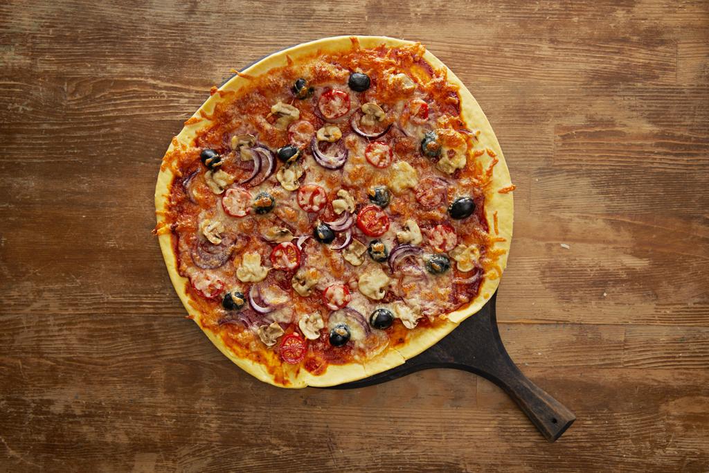 Top view of delicious pizza with cherry tomatoes, olives and parmesan on cutting board on wooden background - 写真・画像