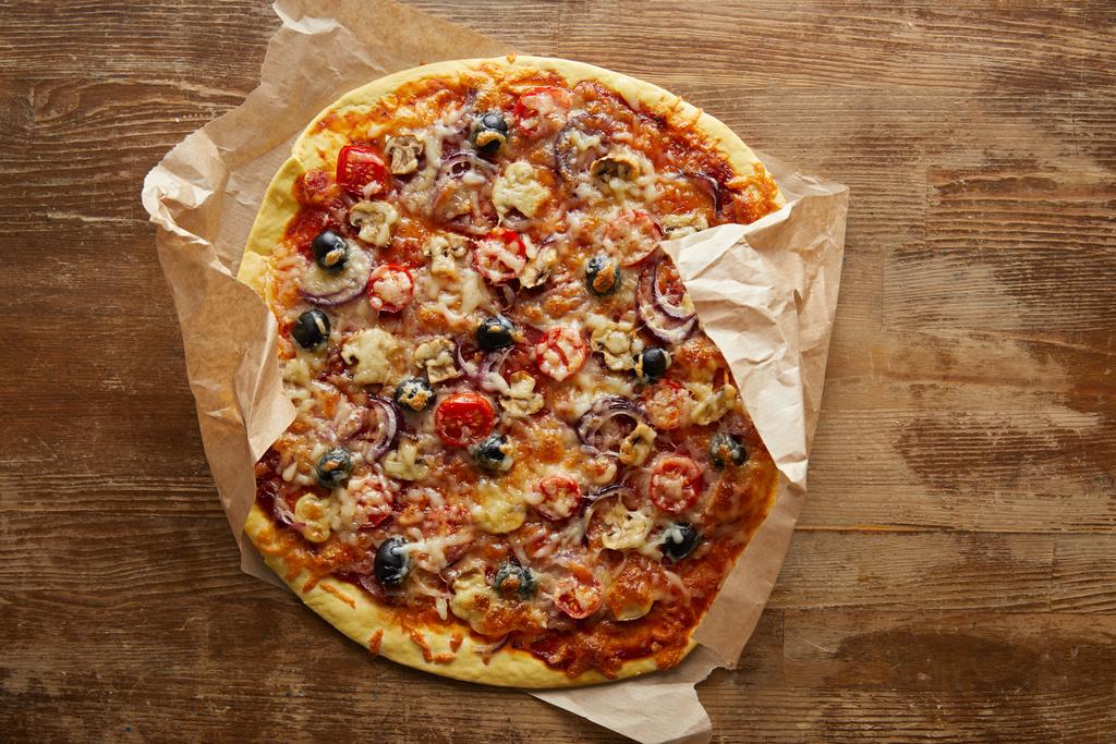 Draufsicht auf leckere Pizza auf Pergamentpapier auf Holzgrund - Foto, Bild