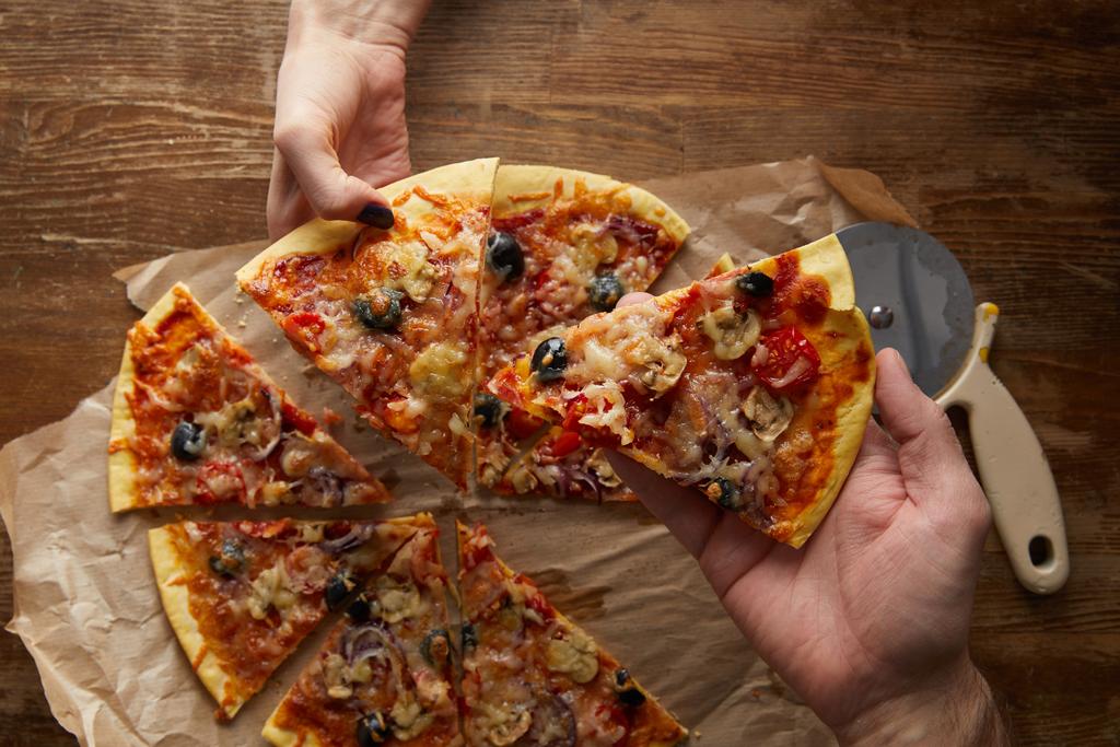 Vista recortada de la pareja comiendo pizza juntos sobre fondo de madera
 - Foto, imagen
