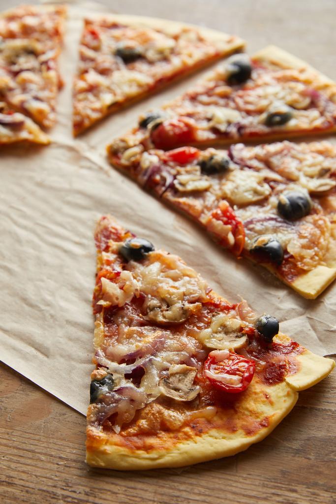 cortar deliciosa pizza italiana con aceitunas sobre papel de hornear sobre fondo de madera
 - Foto, Imagen