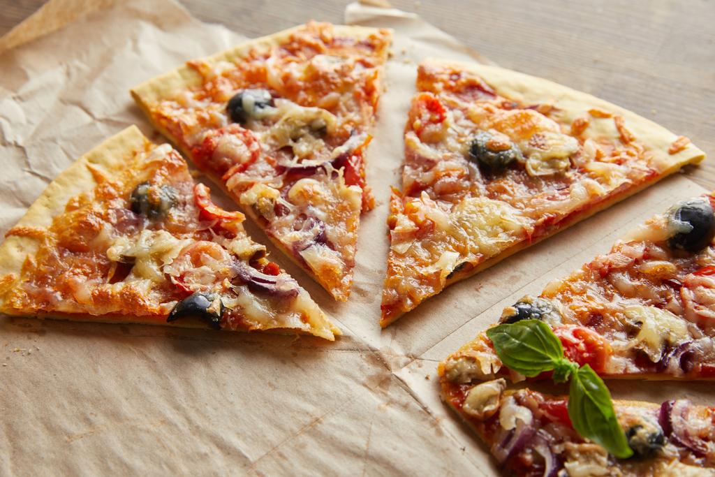 κομμένα νόστιμα ιταλική πίτσα με ελιές σε χαρτί ψησίματος σε ξύλινο τραπέζι - Φωτογραφία, εικόνα