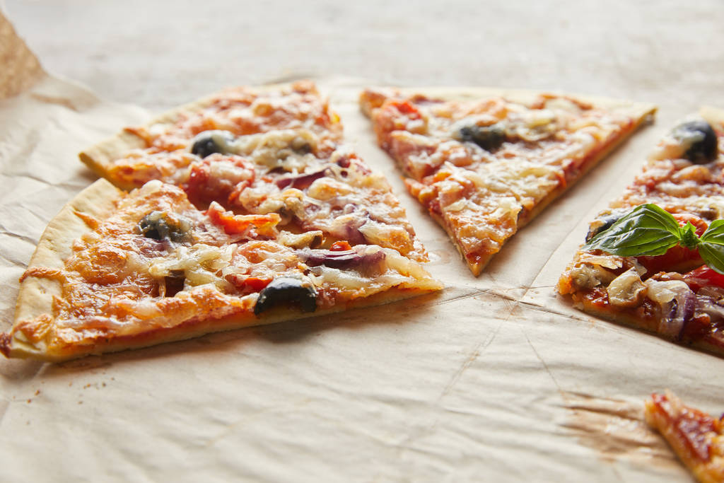 wyciąć pyszną włoską pizzę z oliwkami na papierze do pieczenia na drewnianym stole - Zdjęcie, obraz