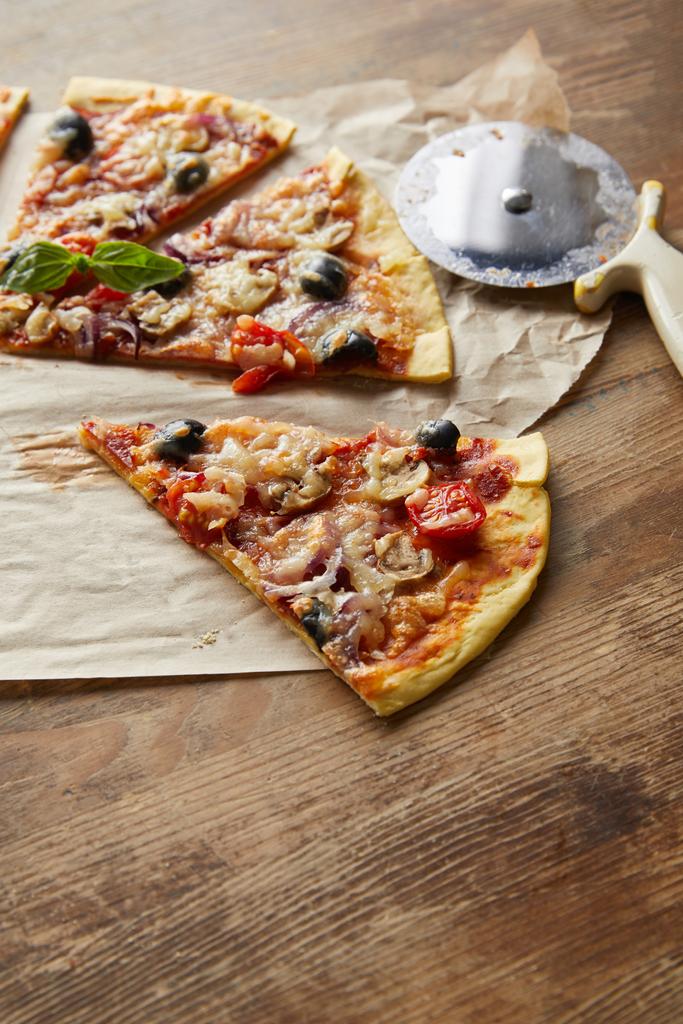 κομμένα νόστιμα ιταλική πίτσα με ελιές σε χαρτί ψησίματος με μαχαίρι πίτσα σε ξύλινο τραπέζι - Φωτογραφία, εικόνα