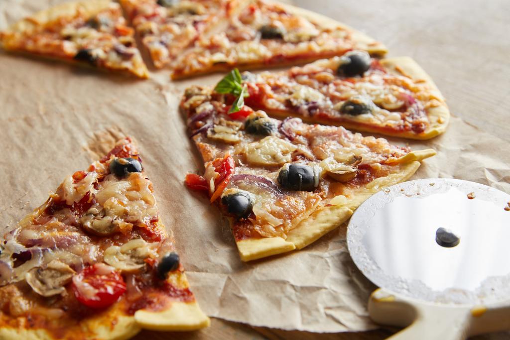 木製のテーブルの上にピザナイフで紙を焼く上でオリーブとカットおいしいイタリアのピザのビューを閉じます - 写真・画像