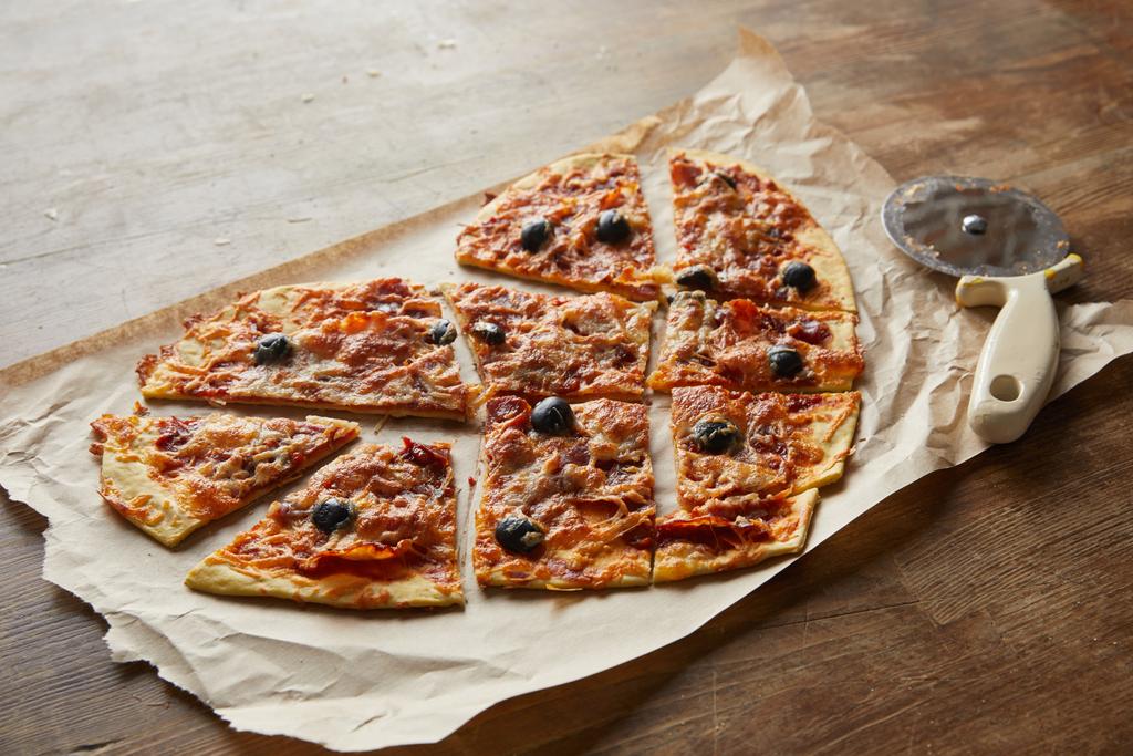 Lezzetli İtalyan pizzası kalp şeklinde. Tahta masada pizza bıçağının yanında kağıt parçalarıyla dilimlenmiş. - Fotoğraf, Görsel