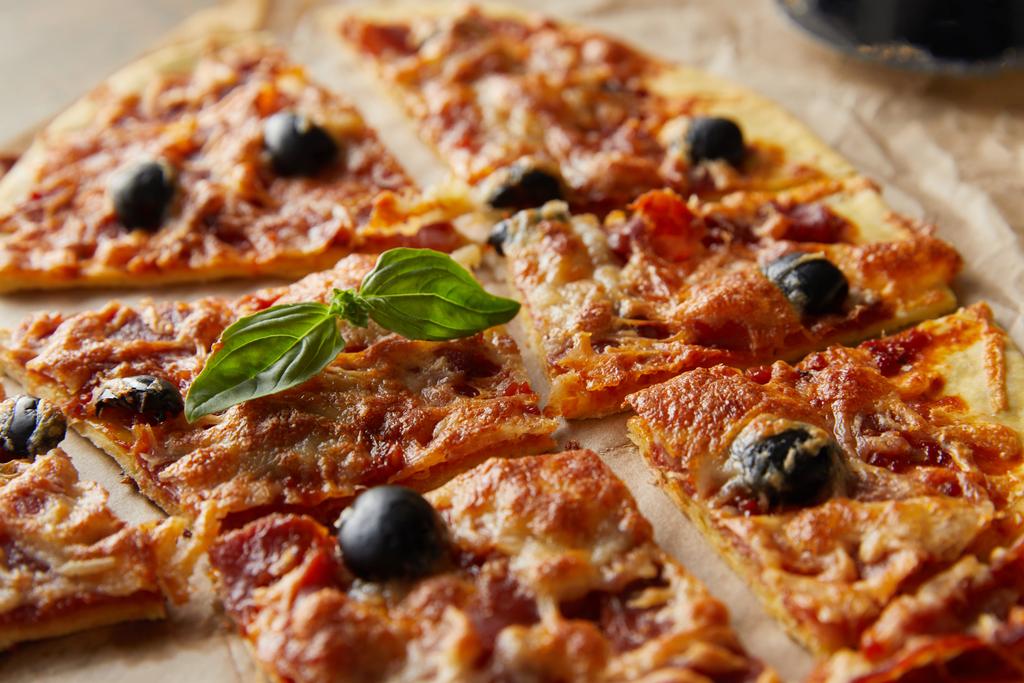 Nahaufnahme der köstlichen italienischen Pizza mit Basilikum in Stücke geschnitten auf Backpapier - Foto, Bild